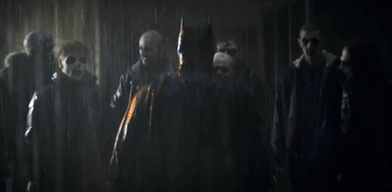 An screenshot of the movie Batman, as Batman stands in the rain in front of a gang of face-painted criminals