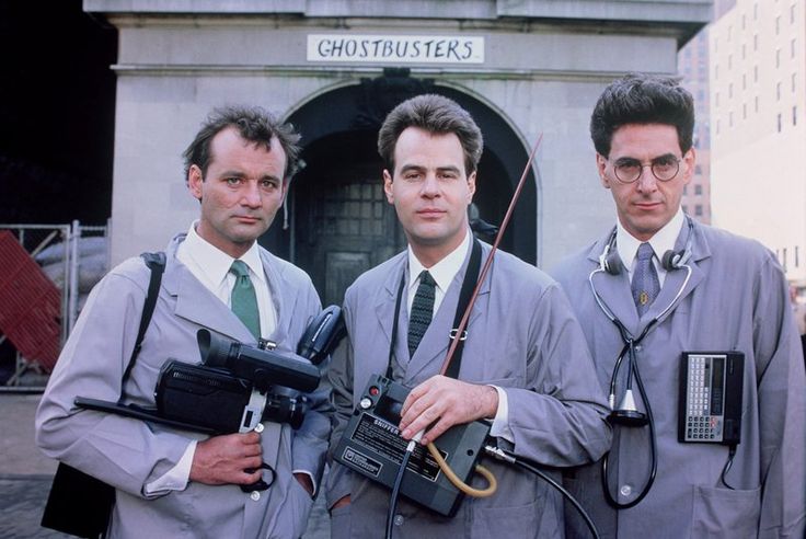 An screenshot of the movie Ghostbusters, as Egon Spengler, Ray Stantz, and Peter venkman stand in front of the Ghostbusters firehouse in scientist clothes