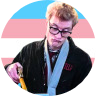 An image of Lars Pinfield (Ghostbusters) in front of a trans flag